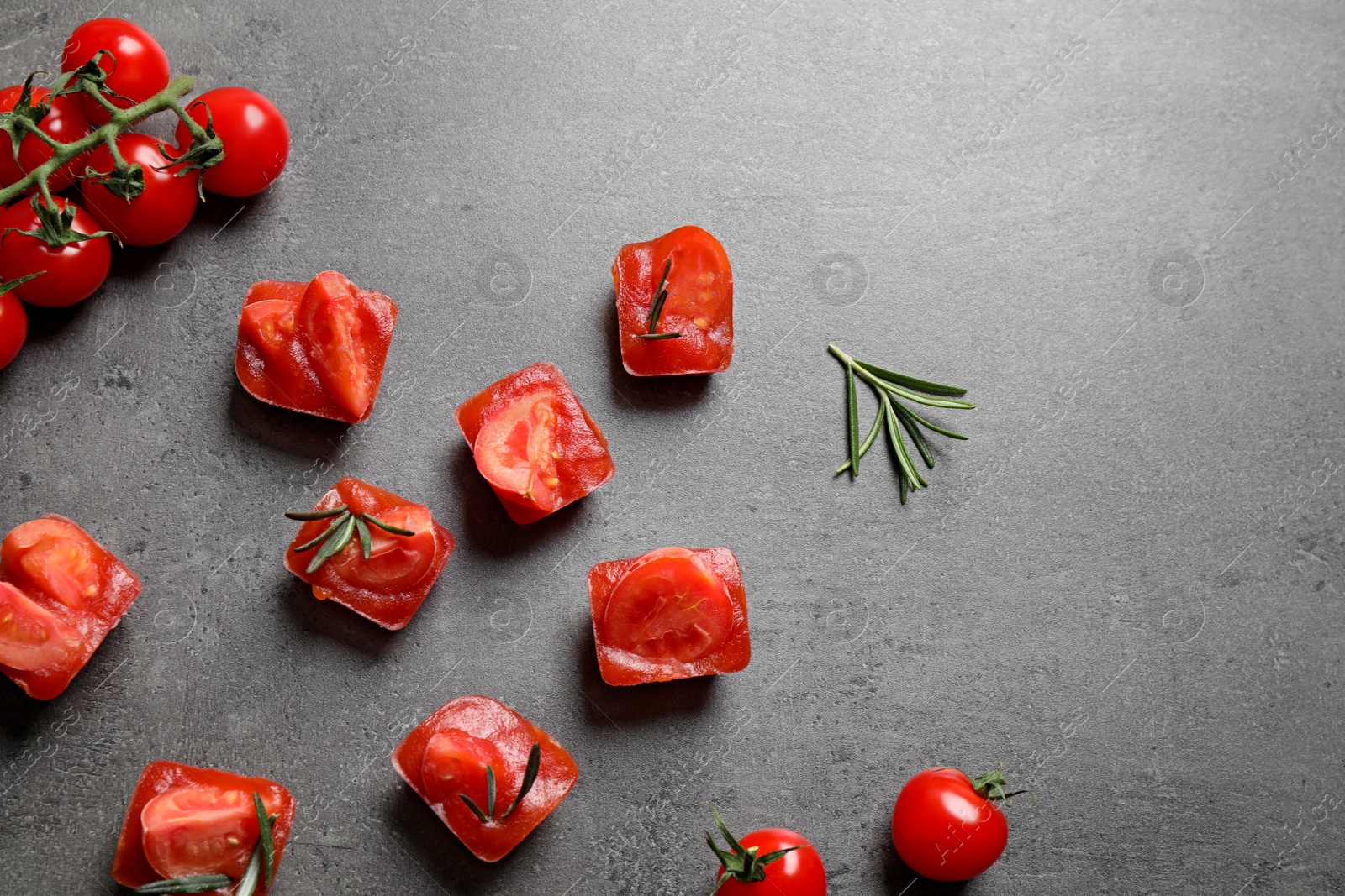 Photo of Ice cubes with tomatoes and rosemary on grey table, flat lay