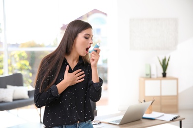 Woman with asthma inhaler in light room