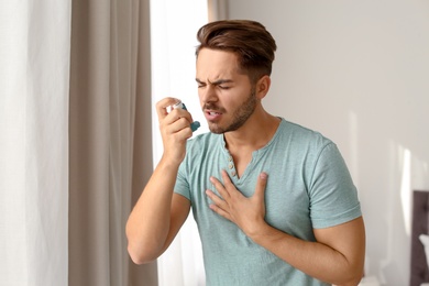 Young man using asthma inhaler at home