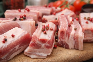 Photo of Cut raw pork ribs with peppercorns on wooden board, closeup