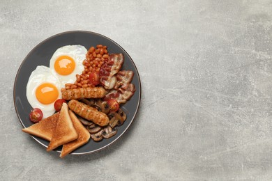 Plate of fried eggs, sausages, mushrooms, beans, bacon and toasted bread on grey table, top view with space for text. Traditional English breakfast