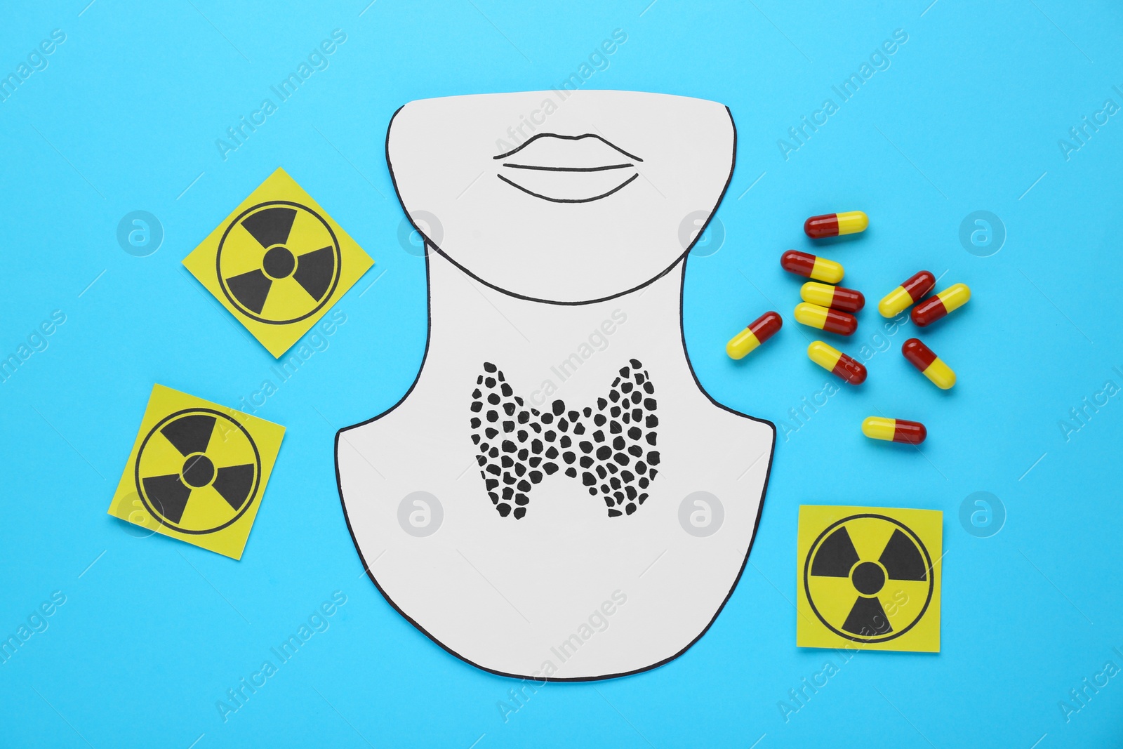 Photo of Paper cutout of thyroid gland, radiation signs and pills on light blue background, flat lay