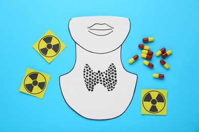 Paper cutout of thyroid gland, radiation signs and pills on light blue background, flat lay