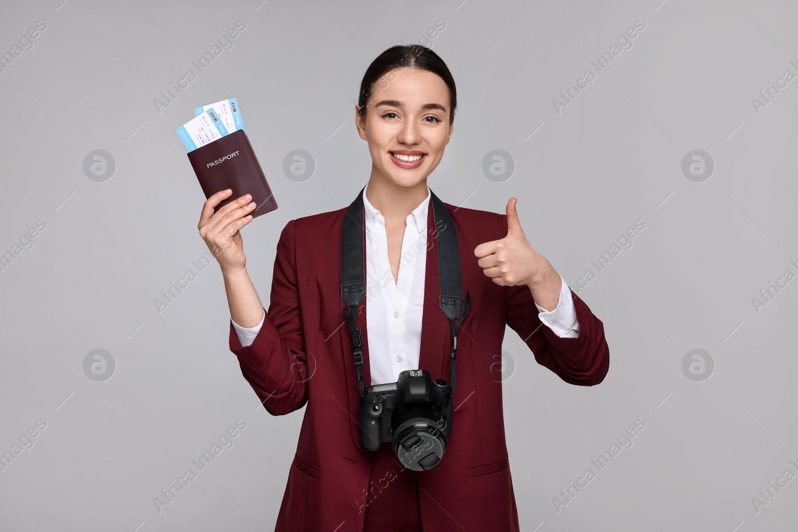 Photo of Smiling businesswoman with passport, tickets and camera showing thumb up on grey background