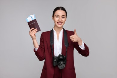 Photo of Smiling businesswoman with passport, tickets and camera showing thumb up on grey background