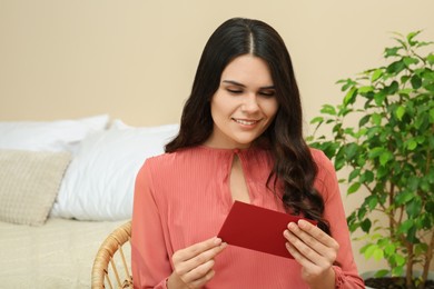 Young woman with greeting card in living room, space for text