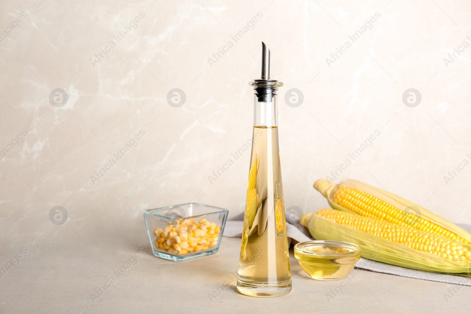 Photo of Bottle of corn oil and fresh cobs on table against light wall