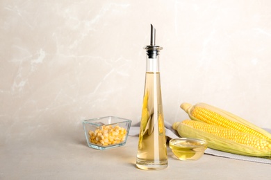 Bottle of corn oil and fresh cobs on table against light wall