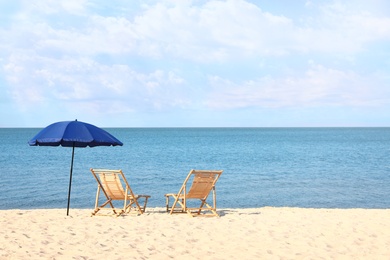 Empty wooden sunbeds and umbrella on sandy shore. Beach accessories