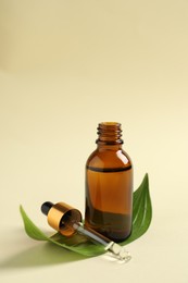 Photo of Bottle of cosmetic oil, pipette and leaf on beige background