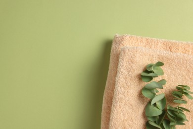 Photo of Soft folded towels with eucalyptus branch on green background, top view. Space for text