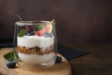 Photo of Glass with yogurt, berries, mint and granola on wooden table, closeup. Space for text