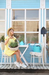 Photo of Young woman with basket of home plants at table near house