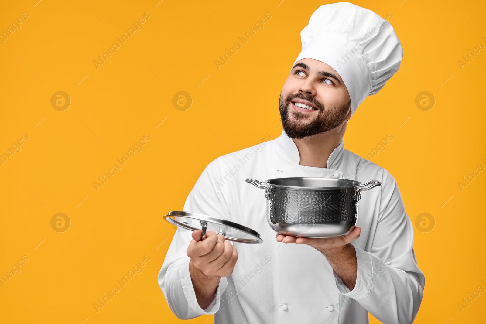 Photo of Happy young chef in uniform holding cooking pot on orange background. Space for text