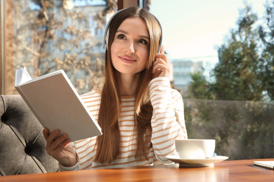 Photo of Woman listening to audiobook at table in cafe