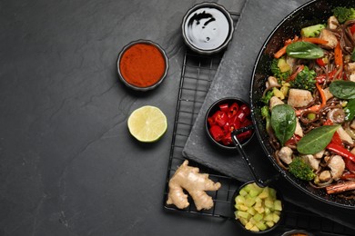 Photo of Stir-fry. Tasty noodles with meat in wok and ingredients on grey textured table, flat lay. Space for text