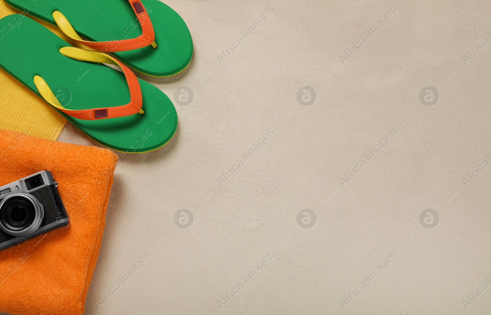 Photo of Beach towel, camera and flip flops on sand, flat lay. Space for text