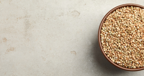 Uncooked green buckwheat grains in bowl on table, top view. Space for text