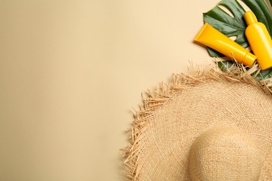 Photo of Straw hat, cosmetic bottles, leaf and space for text on beige background, flat lay. Stylish headdress