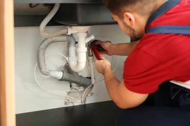 Male plumber repairing kitchen sink with pipe wrench