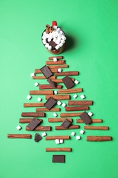 Christmas tree made with marshmallows, cinnamon and chocolate on green background, flat lay