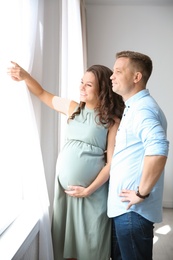 Photo of Pregnant woman with her husband looking out of window. Future parents concept