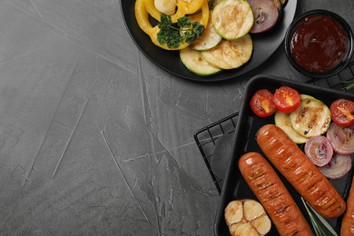 Photo of Delicious grilled sausages and vegetables on grey table, flat lay. Space for text