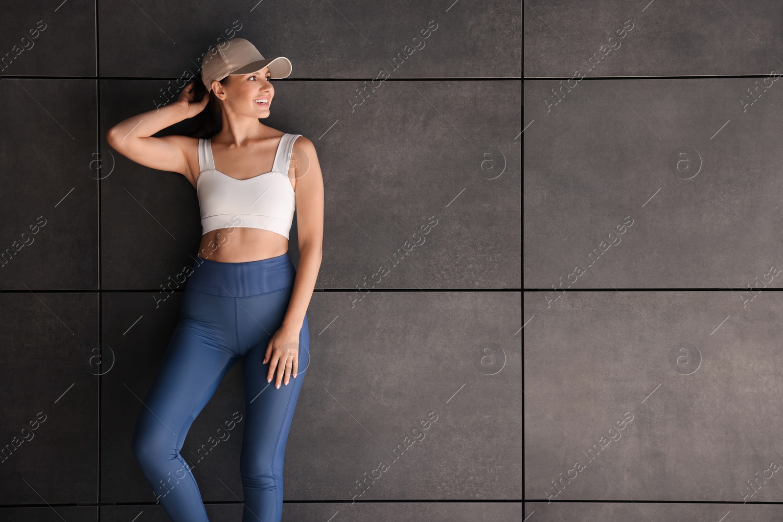 Photo of Smiling woman in sportswear near dark grey wall. Space for text
