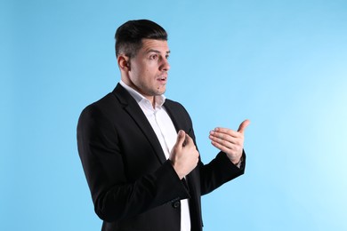 Emotional man in suit pointing at himself on light blue background