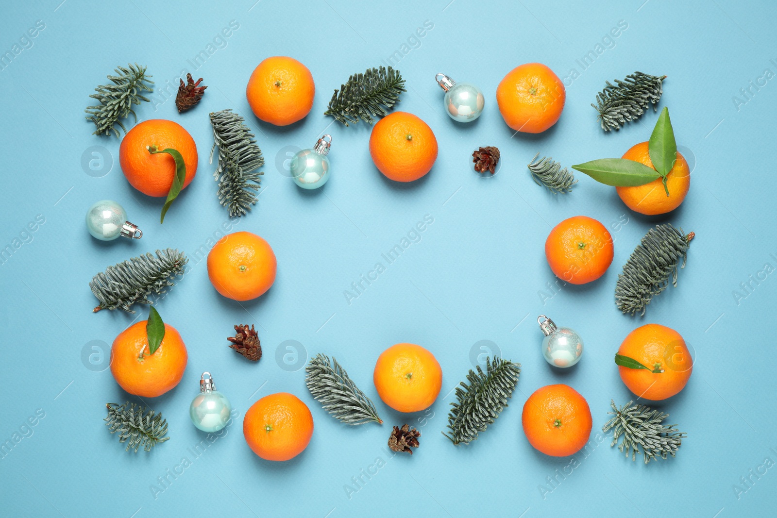 Photo of Frame made of Christmas balls and tangerines on light blue background, flat lay