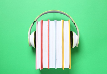 Books with modern headphones on green background, top view