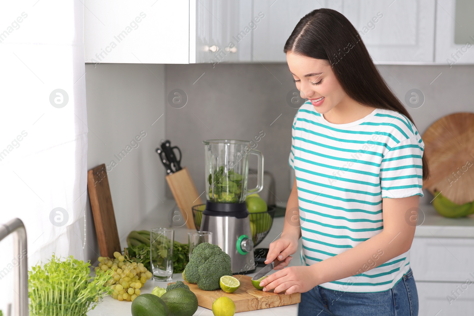 Photo of Young woman cutting lime for smoothie in kitchen