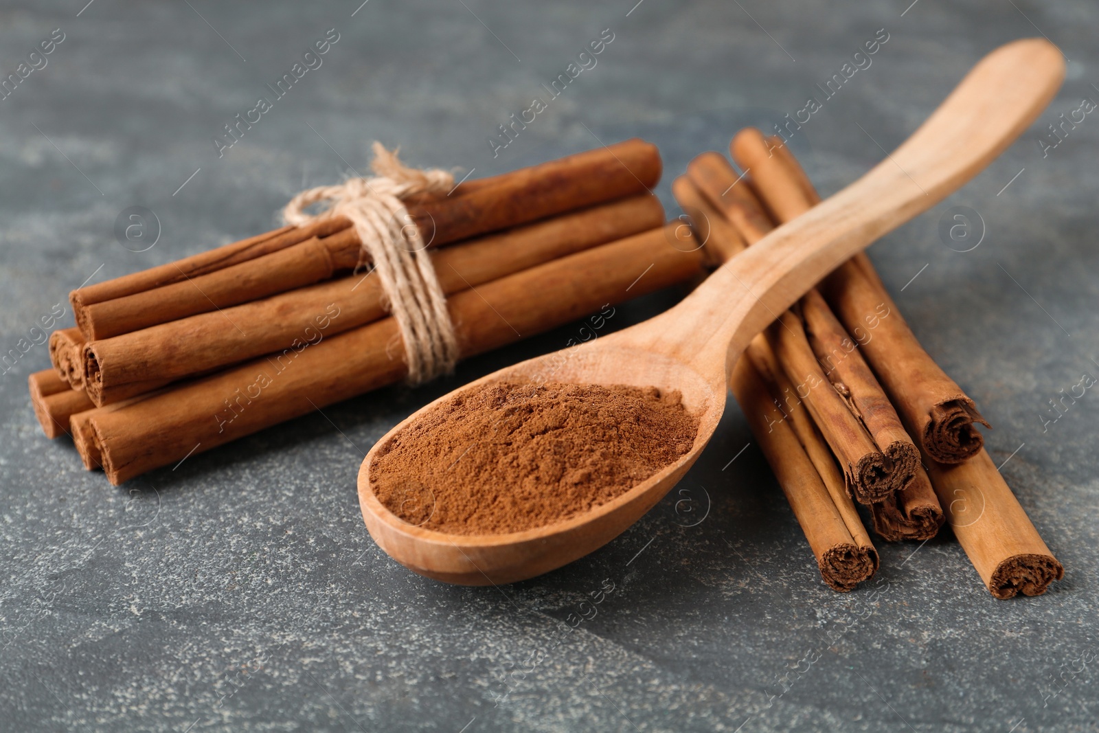 Photo of Aromatic cinnamon powder and sticks on grey table, closeup