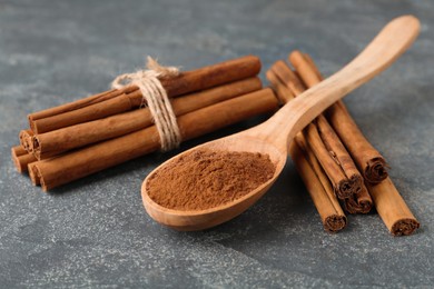 Aromatic cinnamon powder and sticks on grey table, closeup