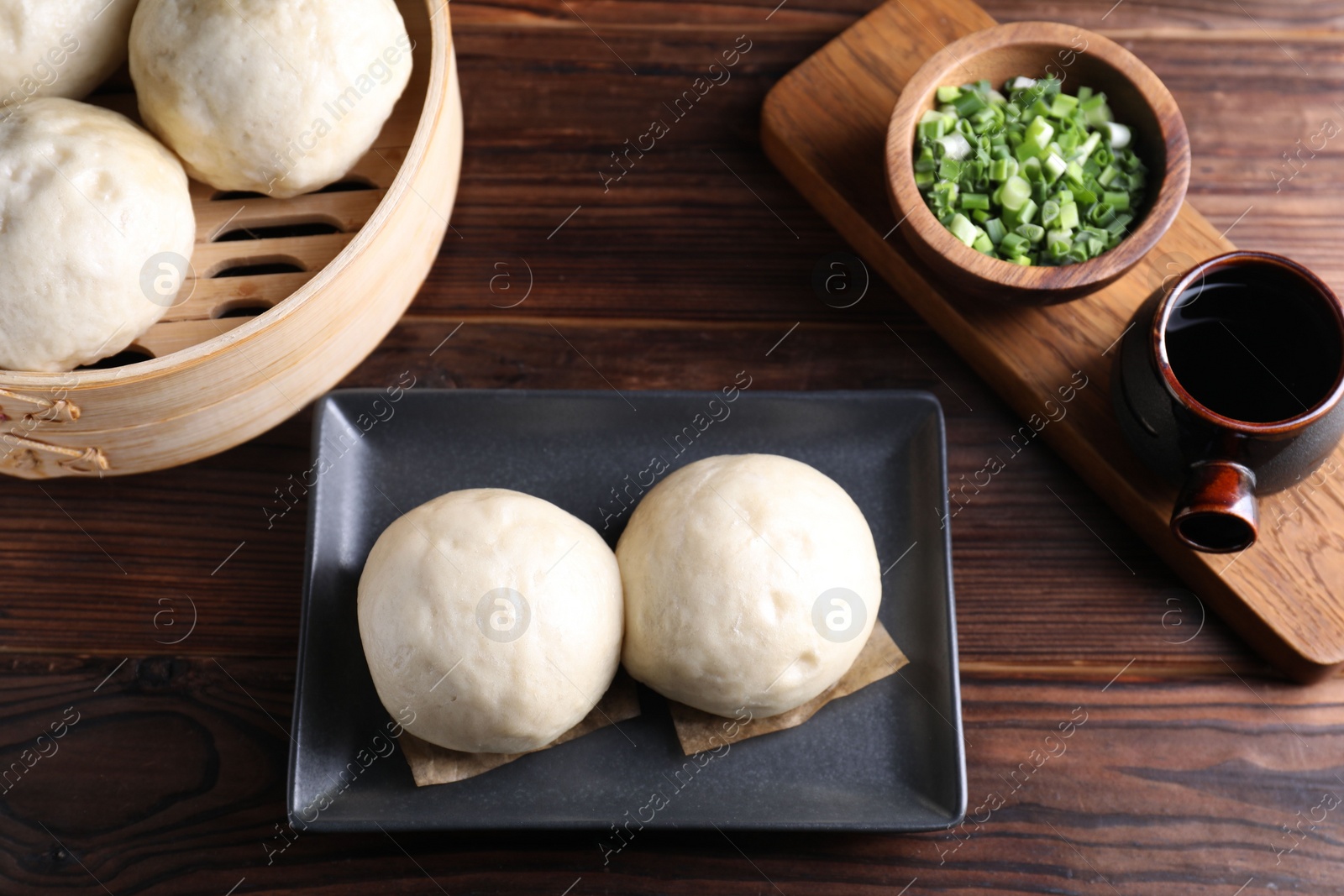 Photo of Delicious Chinese steamed buns, green onion and soy sauce on wooden table, flat lay