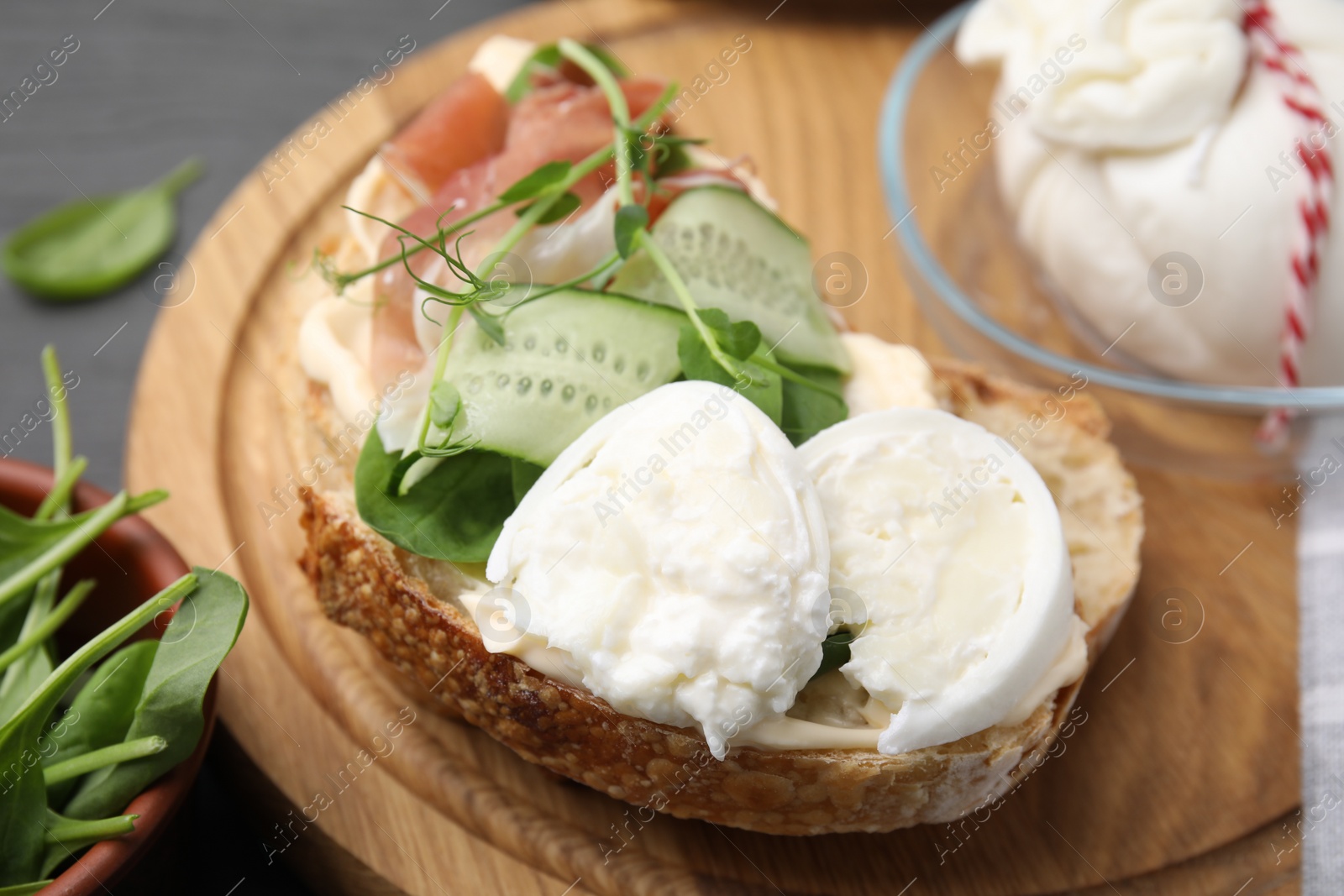 Photo of Tasty sandwich with burrata cheese, prosciutto and cucumber on table, closeup