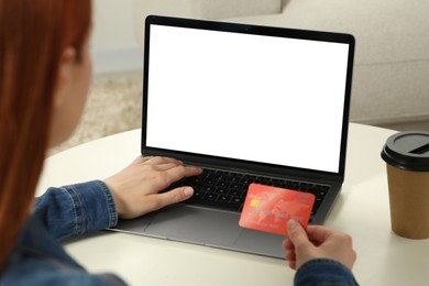 Woman with credit card using laptop at white table indoors, closeup