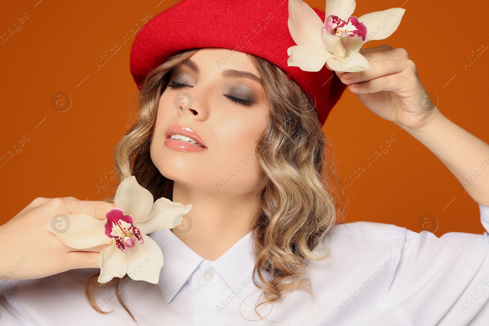 Photo of Portrait of young woman with beautiful orchid flowers on orange background, closeup