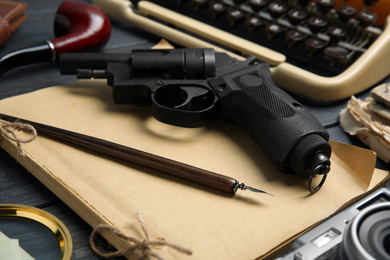 Photo of Revolver, ink pen and vintage notebook on grey wooden table, closeup. Detective's workplace