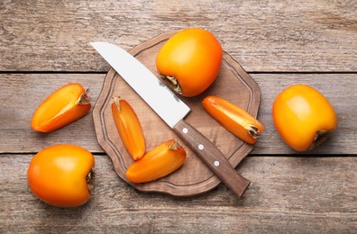 Photo of Delicious ripe persimmons and knife on wooden table, flat lay