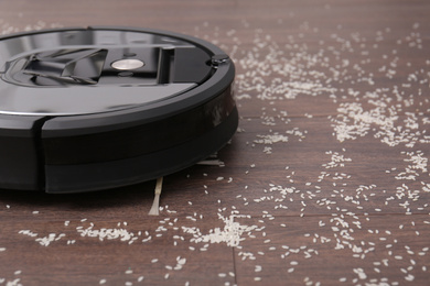 Removing groats from wooden floor with robotic vacuum cleaner at home, closeup