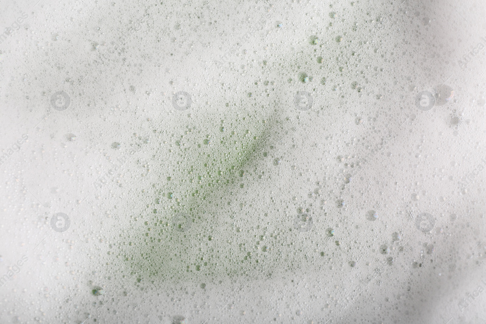 Photo of White fluffy foam on green background, top view