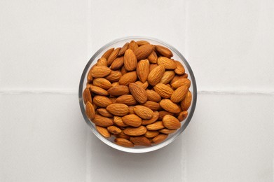 Bowl of delicious almonds on white tiled table, top view