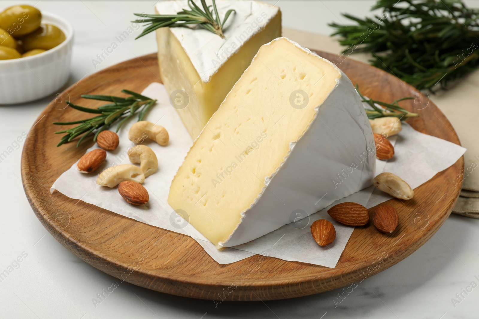 Photo of Plate with pieces of tasty camembert cheese, nuts and rosemary on white table, closeup