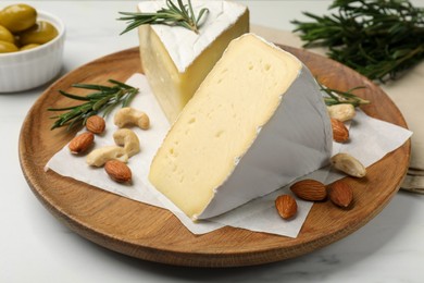 Plate with pieces of tasty camembert cheese, nuts and rosemary on white table, closeup