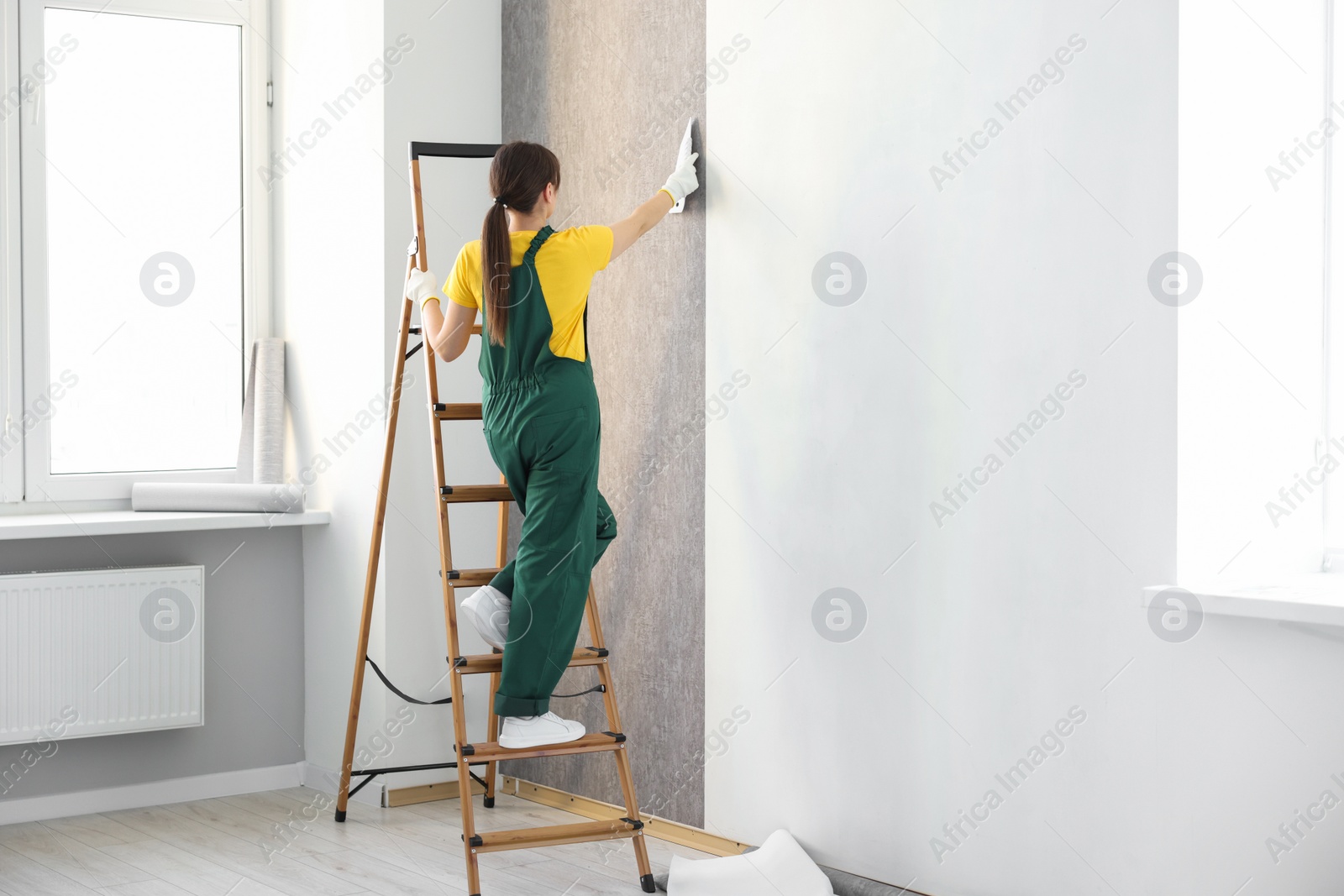 Photo of Woman smoothing stylish gray wallpaper in room