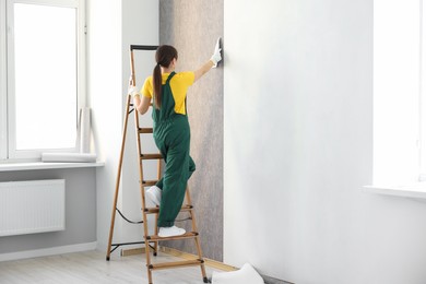 Photo of Woman smoothing stylish gray wallpaper in room