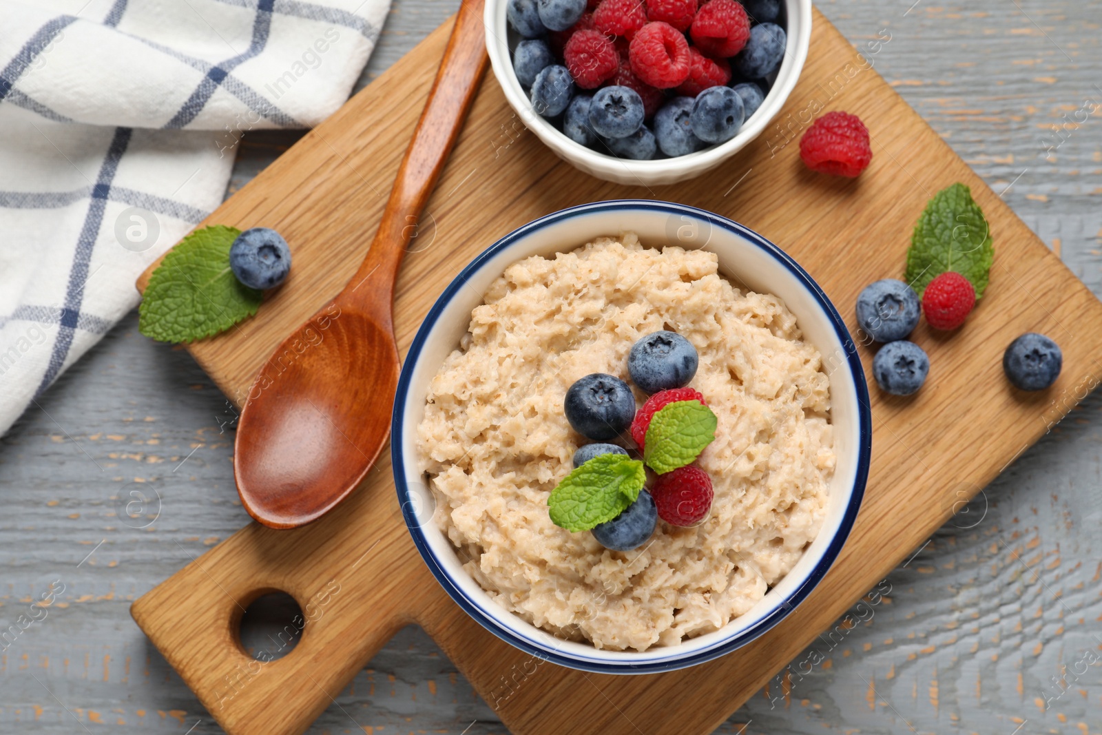 Photo of Tasty oatmeal porridge with berries on grey wooden table, flat lay