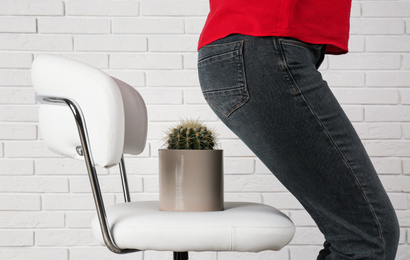 Woman sitting down on chair with cactus near white brick wall, closeup. Hemorrhoids concept