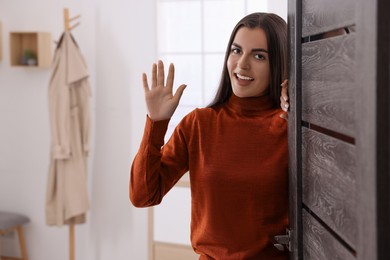 Photo of Happy woman waving near door, space for text. Invitation to come indoors